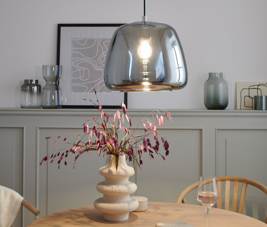 Chrom-Pendelleuchte über einem Tisch mit Vase und Weinglas.