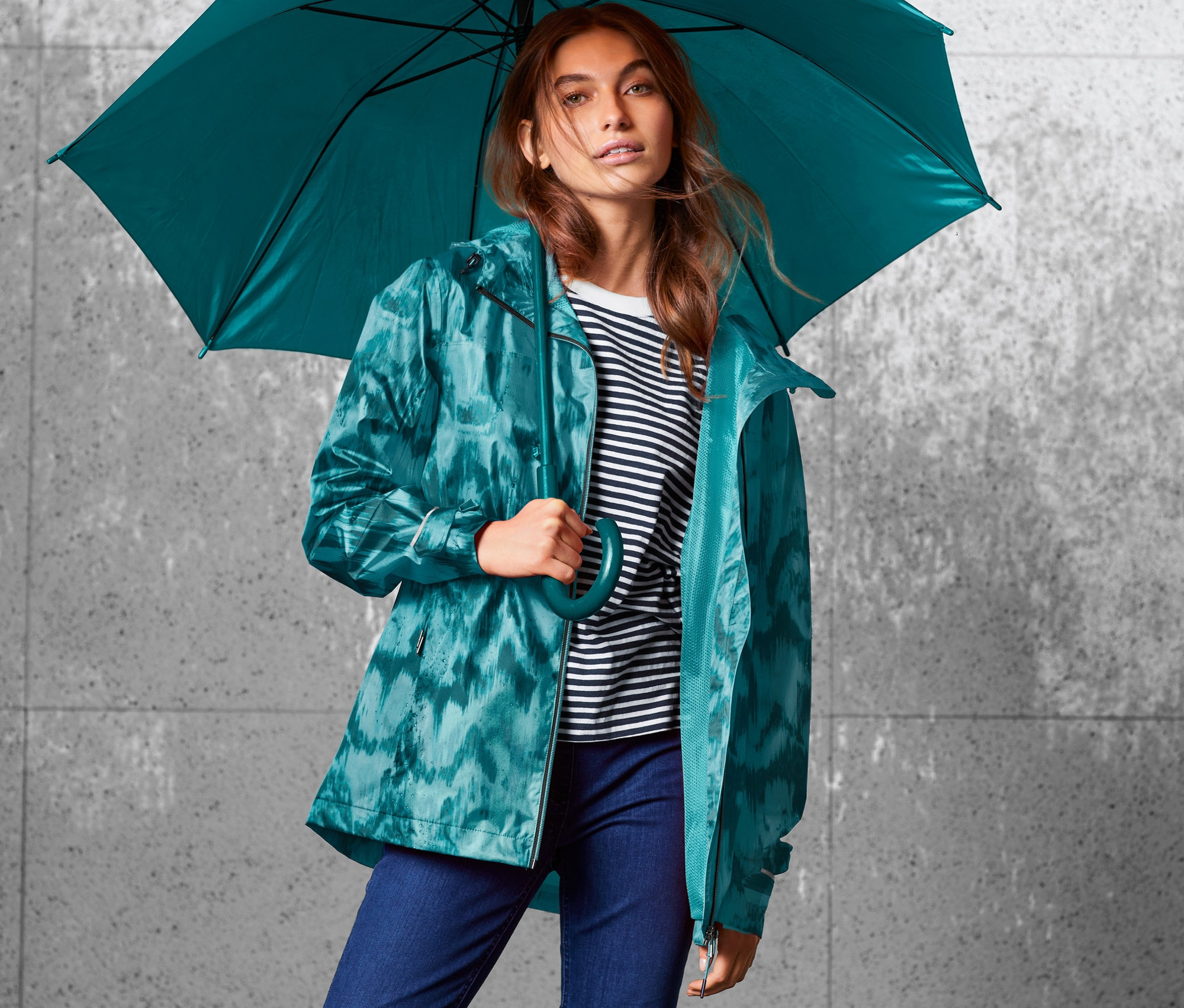 Frau hält einen Regenschirm und trägt eine Regenjacke mit Alloverprint.