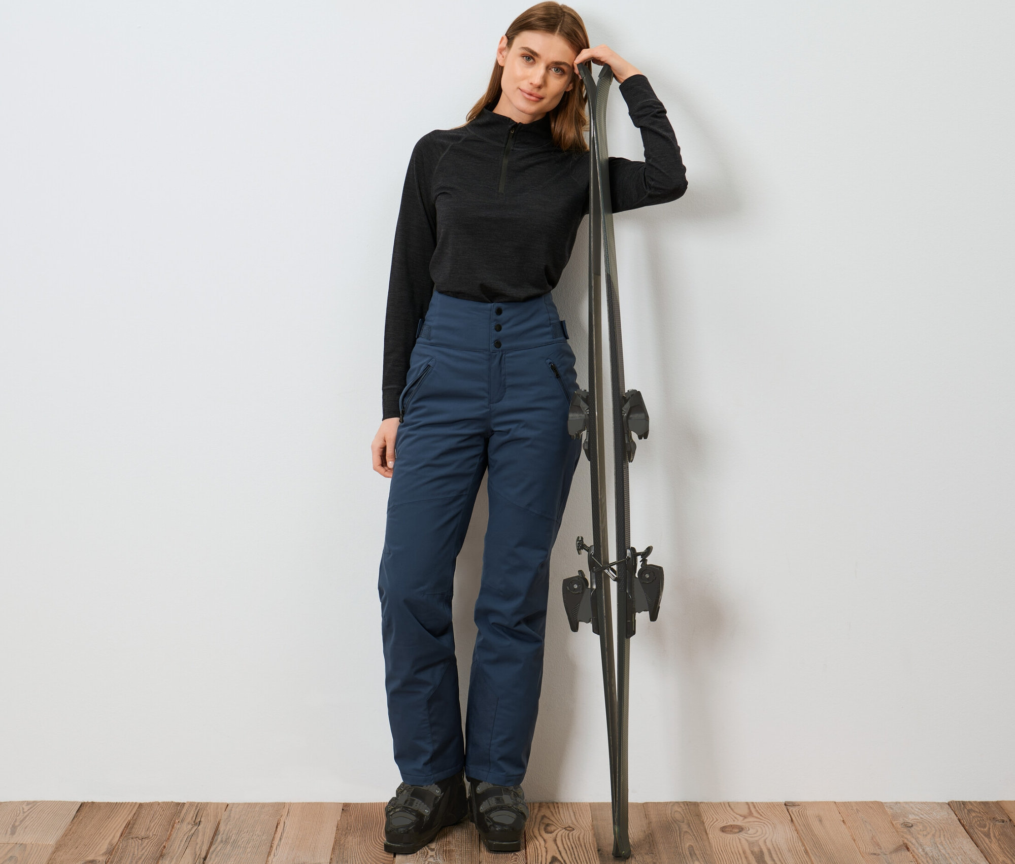 Frau lehnt an Ski und trägt eine blaue High-Waist-Skihose.