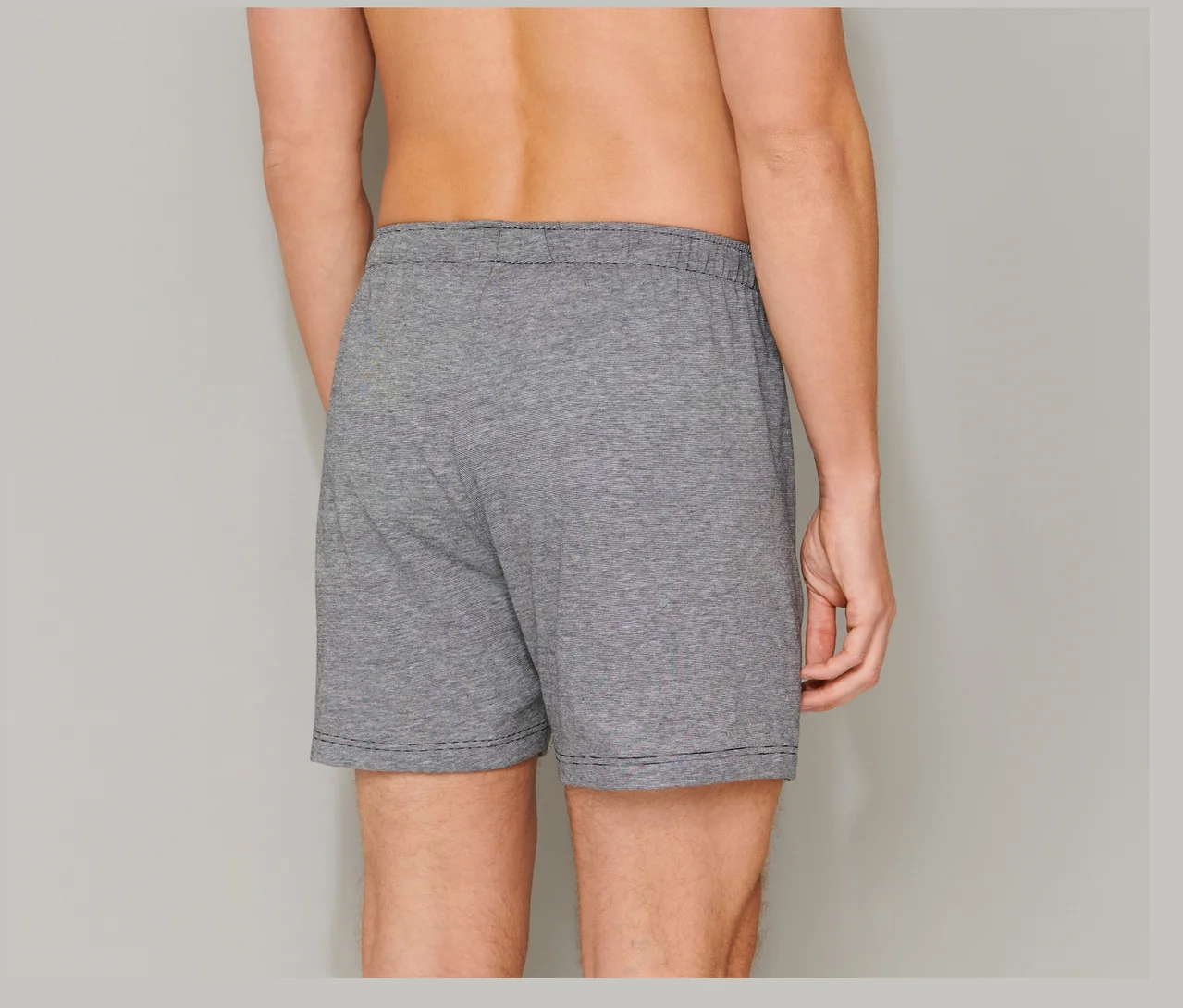 Mann von hinten in grauen SCHIESSER Boxershorts aus Baumwolle mit elastischem Bund und schwarzer Naht am Saum.