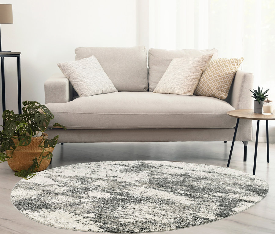 Wohnzimmer mit beigem Sofa, rundem grauem Teppich und Pflanze im Korb.