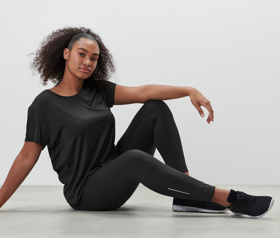 Frau sitzt in schwarzer Sporttight und schwarzem Funktionsshirt auf dem Boden.