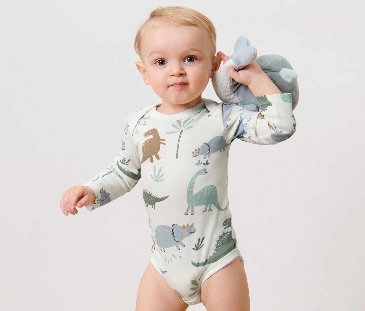 Ein Baby hält ein Stofftier und trägt einen 3 Langarmbodys, Dino.