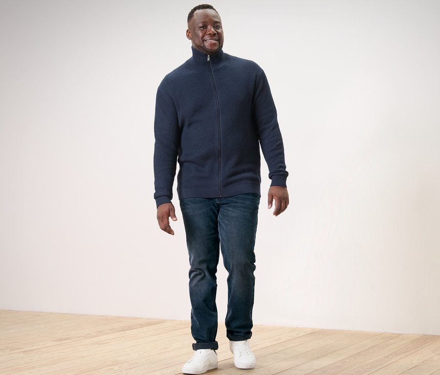 Mann geht und trägt eine Strickjacke in Navy, Jeans und Turnschuhe.