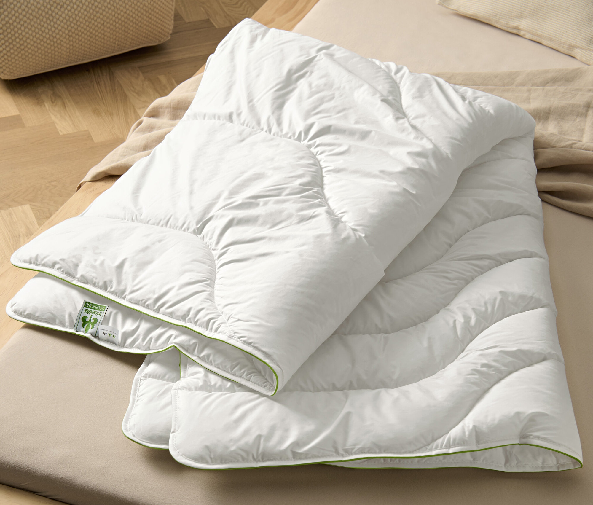 Eine weiße irisette® greenline Steppdecke Megafil® BIO liegt auf einem Bett.