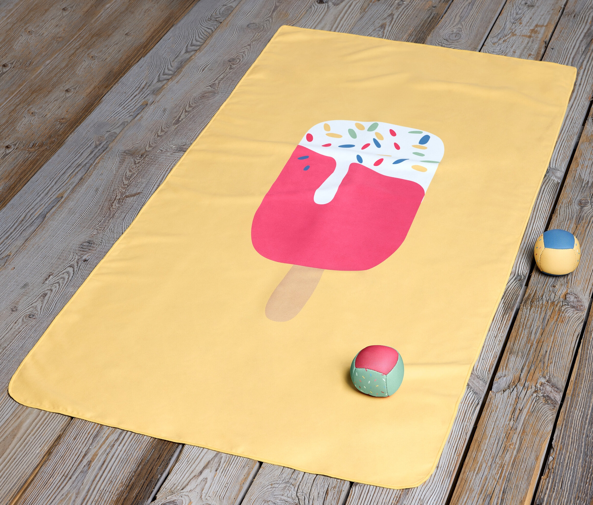 Ein gelbes Kinder-Microfaserhandtuch mit Eis liegt auf einem Holzboden.