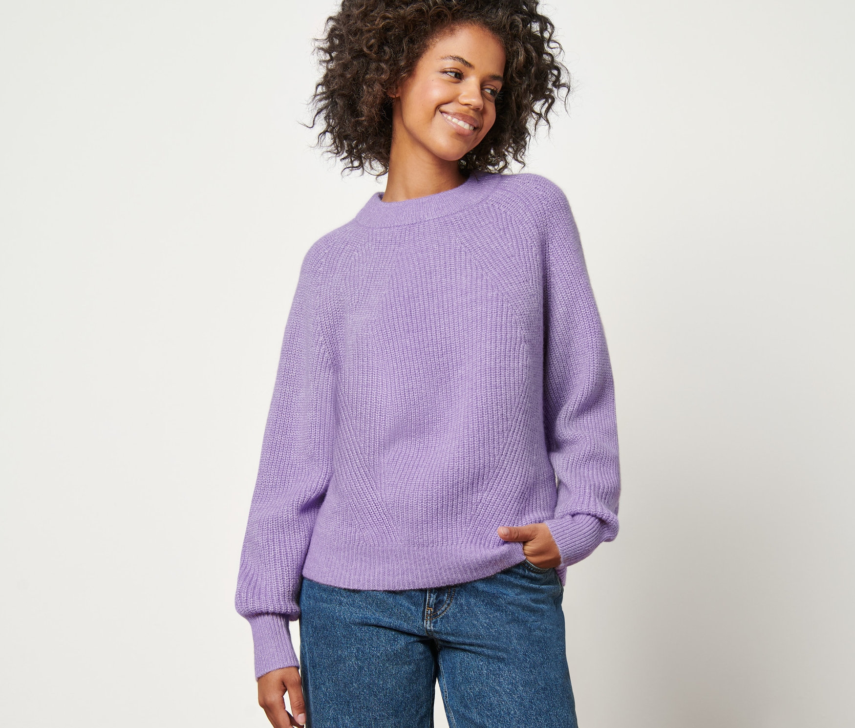 Frau posiert in Strickpullover und Jeans.