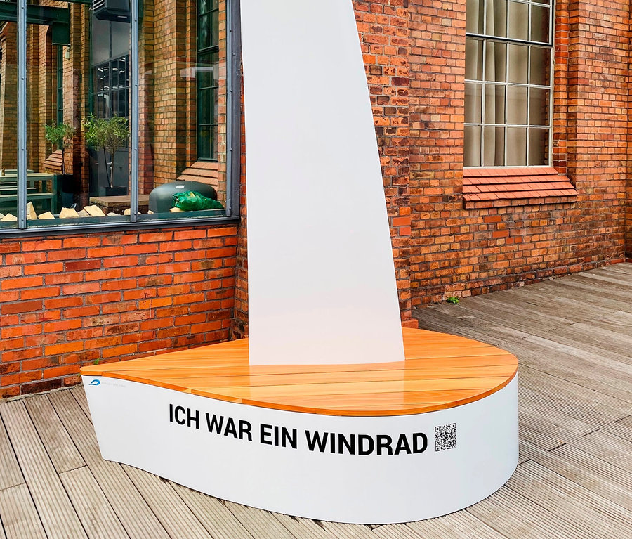 Eine weiße Wings for Living Bank »Sydney« steht im Freien vor einem Backsteingebäude.