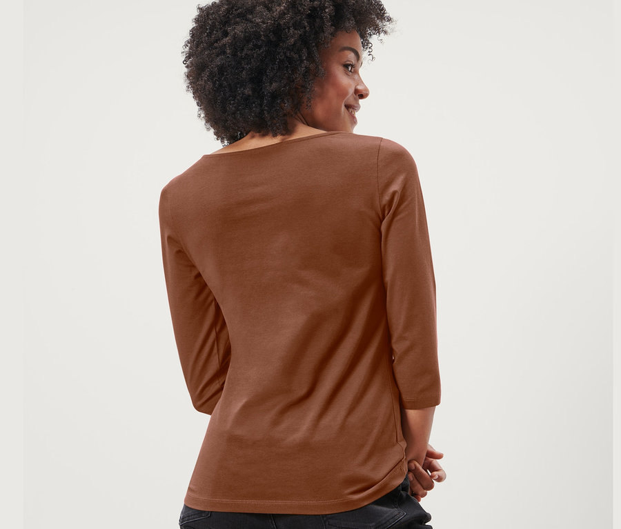 Rückansicht einer Frau mit Afro, die ein cognacfarbenes Shirt mit 3/4-Arm und schwarze Jeans trägt.