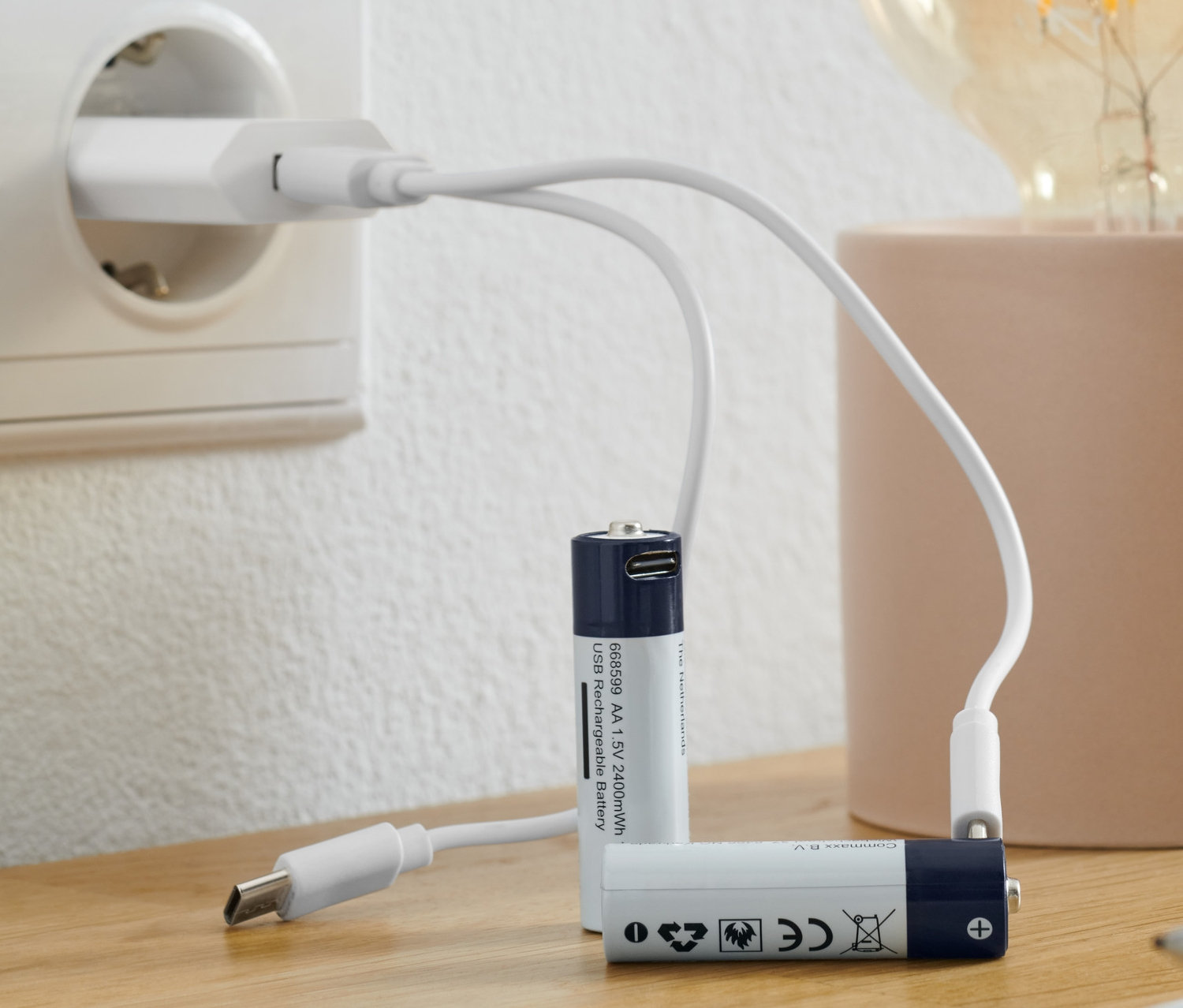 Akku AA-Batterien werden mit einem USB-Kabel, das in eine Steckdose gesteckt ist, neben einer Lampe aufgeladen.
