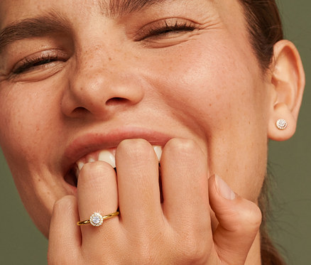 Lächelnde Frau mit einem Ring und Ohrsteckern aus 375 Gold mit Diamanten.