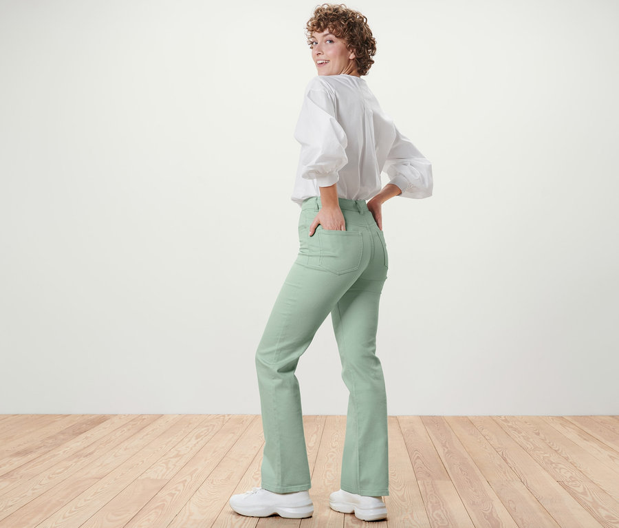 Frau blickt über die Schulter und posiert in mintgrünen Bootcut Jeans – Fit »Lou« und weißer Bluse.
