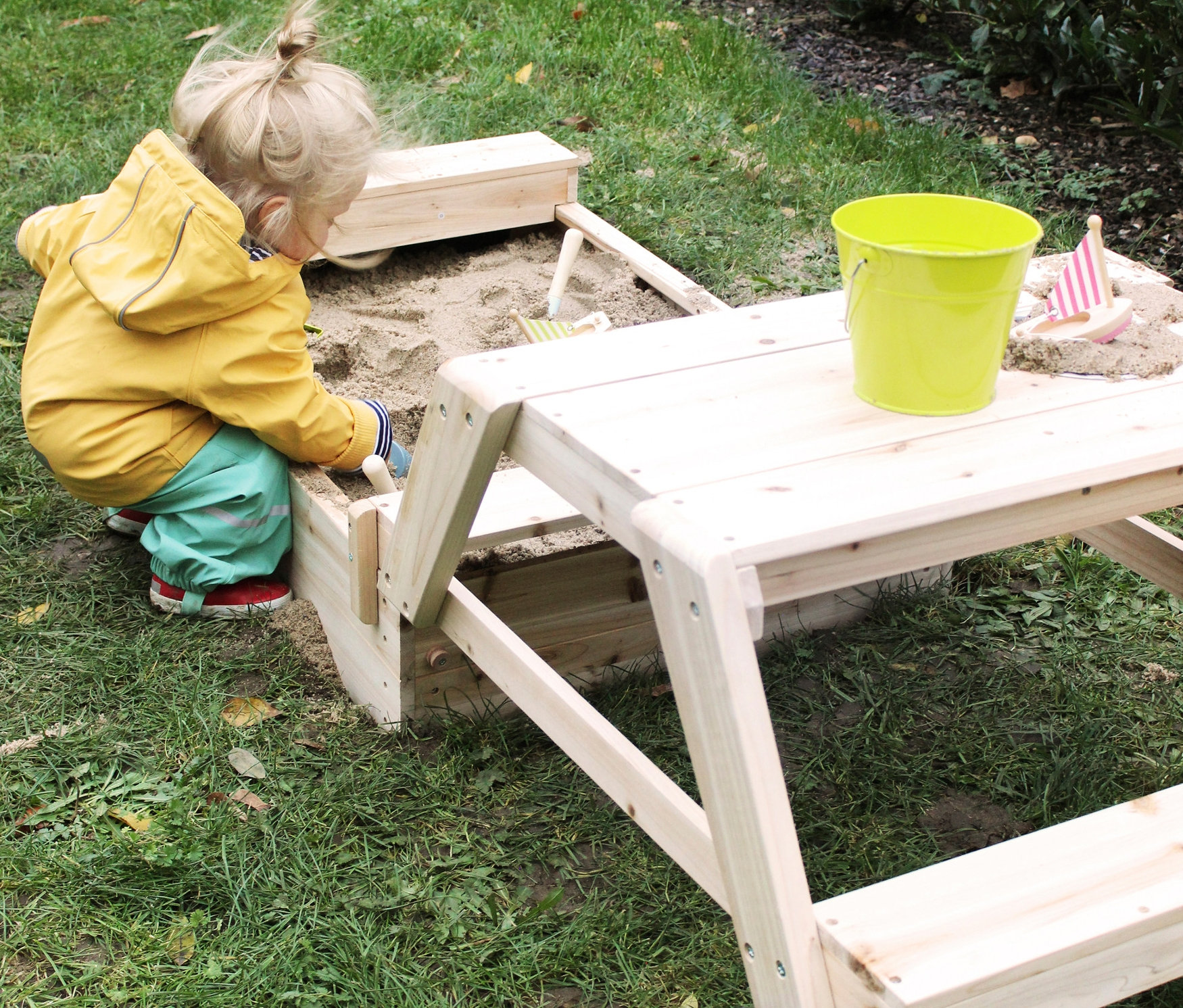 Kind spielt im small foot Sandkasten mit Sitzgruppe und Matschtisch.