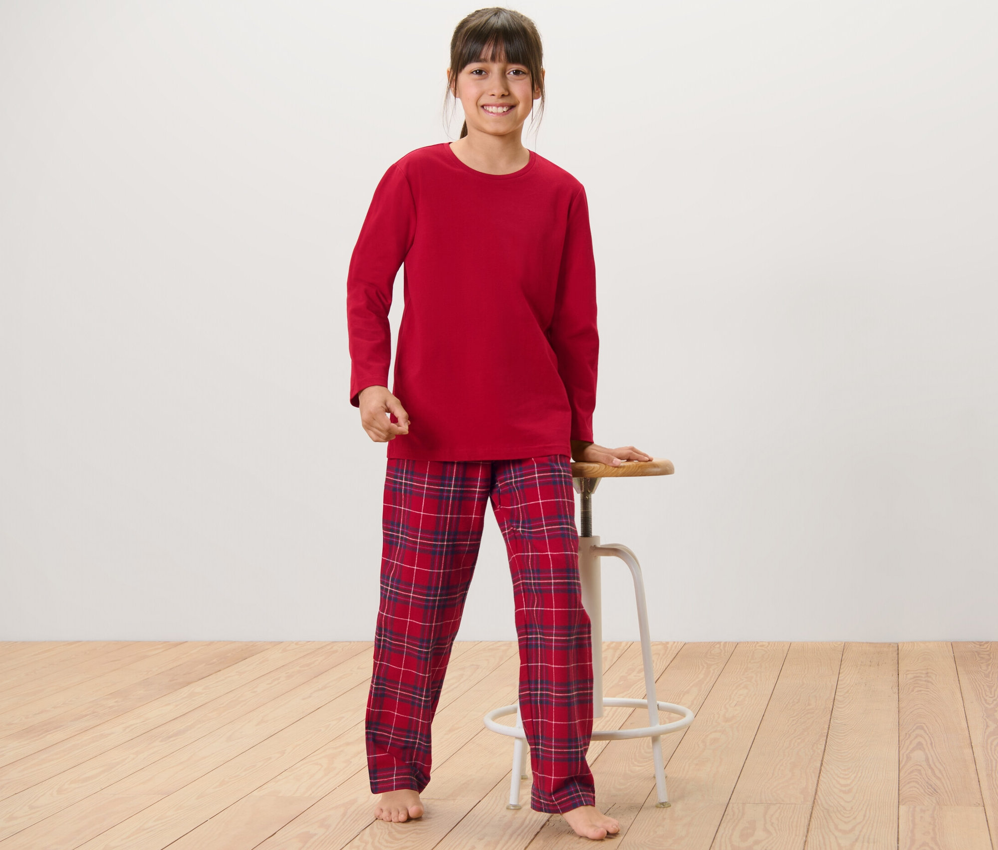 Mädchen steht und lehnt sich an einen Hocker, sie trägt einen Kinder-Flanell-Pyjama.
