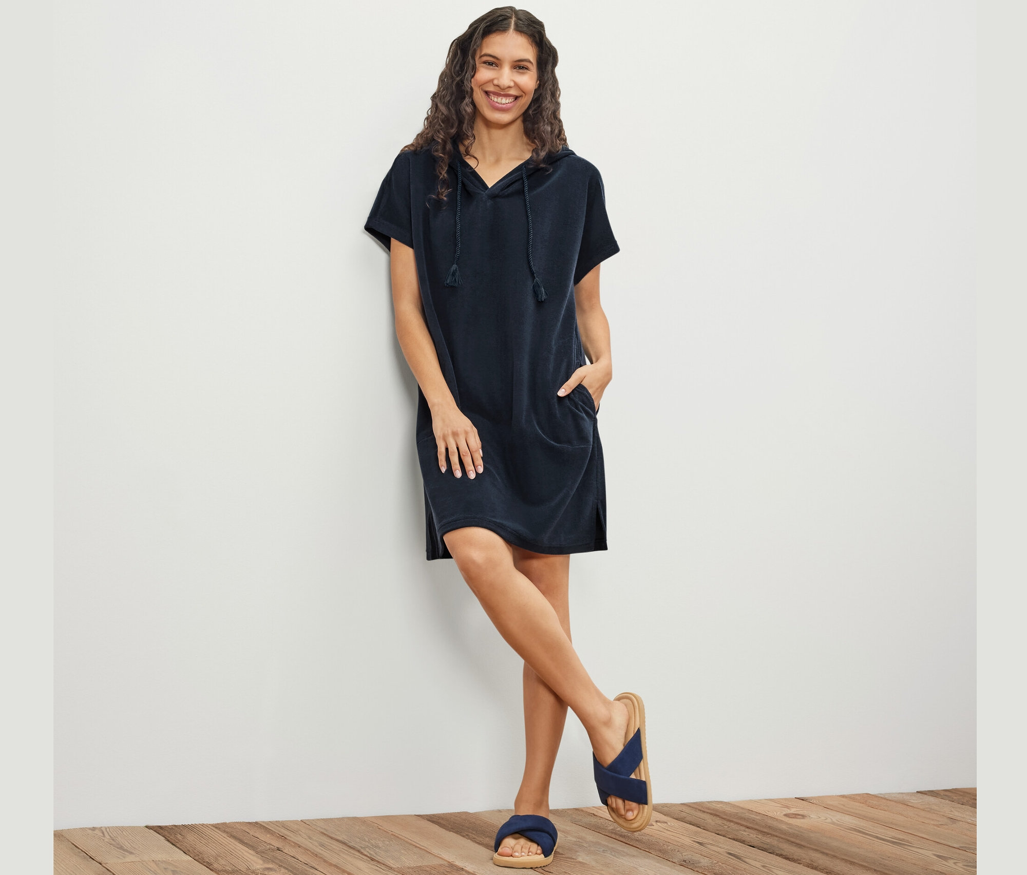 Frau posiert an einer Wand, sie trägt ein blaues Frottee-Strandkleid.