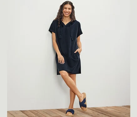 Frau posiert an einer Wand, sie trägt ein blaues Frottee-Strandkleid.