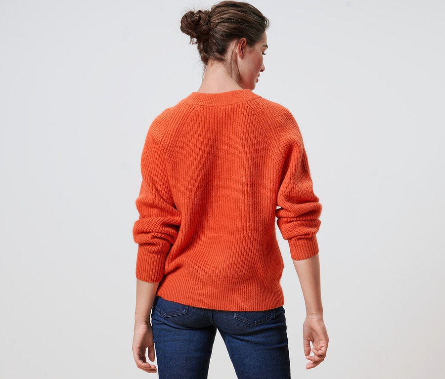 Rückansicht einer Frau mit einem orangefarbenen Strickpullover und Jeans.