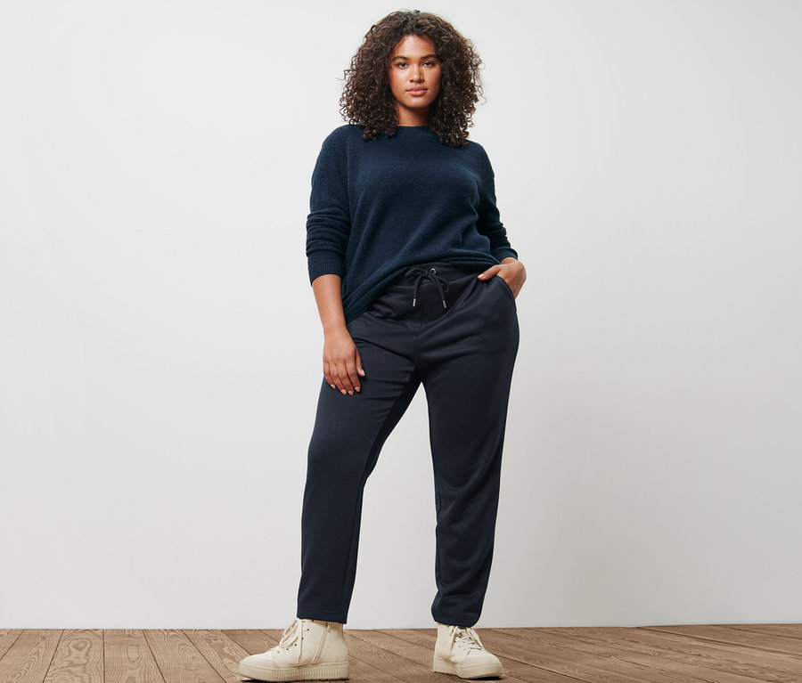 Frau posiert in Strickpullover in Boucléoptik und dunkelblauer Joggpants.