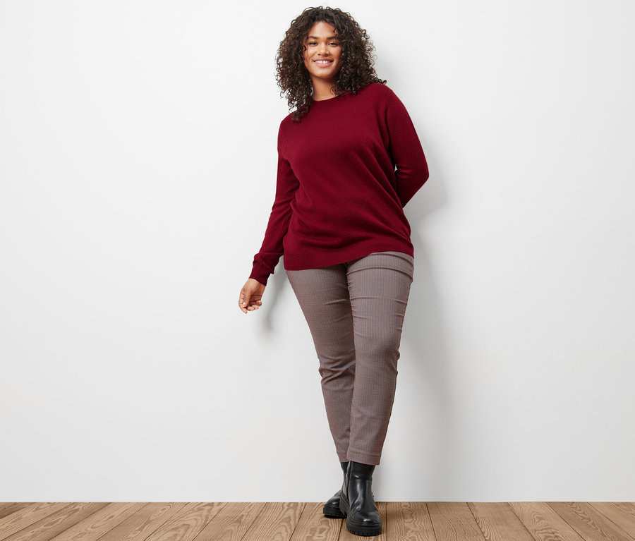 Frau trägt einen bordeauxroten Feinstrickpullover mit Cashmere und eine karierte Stretchhose.