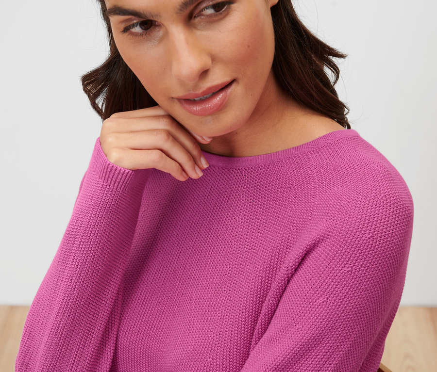 Frau berührt ihr Gesicht und trägt einen pinken Strickpullover.