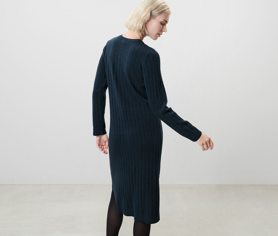 Blonde Frau posiert in geripptem, dunkelblauem Strickkleid.