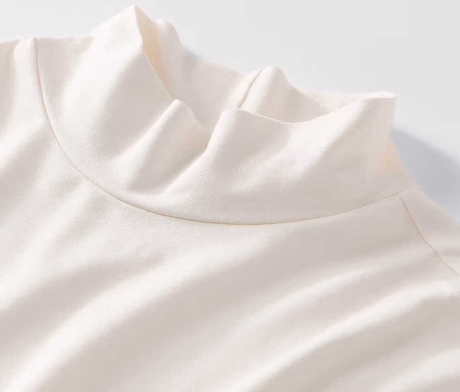 Detailansicht eines cremefarbenen Blusenshirts mit Stehkragen auf weißem Hintergrund.