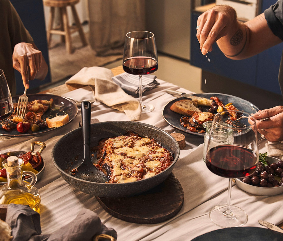 Zwei Personen essen am Tisch mit Rotwein und einem BALLARINI Torre Aluminium-Bratpfannen-Set.