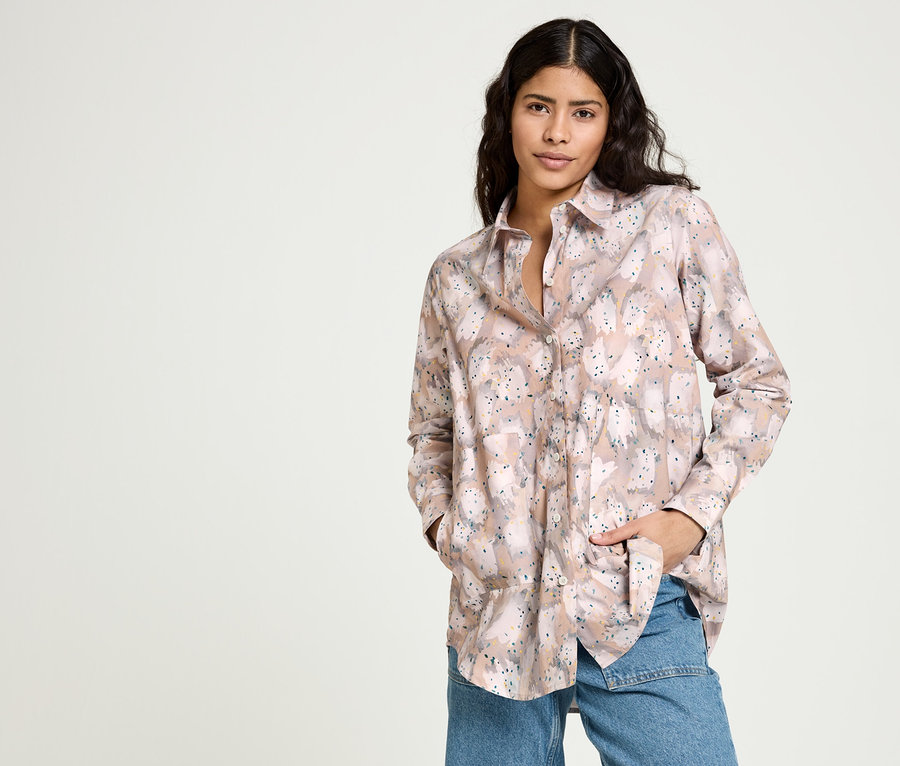 Frau posiert in NAH/STUDIO Mom-Jeans aus recycelter Baumwolle, Mid Blue und NAH/STUDIO Longbluse aus Bio-Baumwolle mit Print.