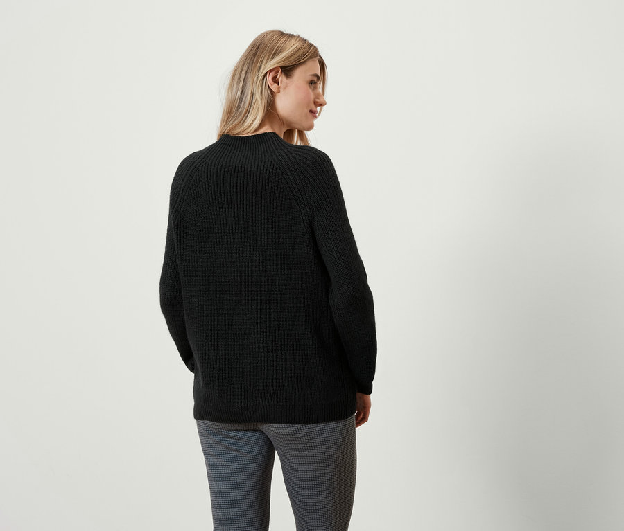 Frau blickt über die Schulter und trägt einen schwarzen Pullover und Hose.