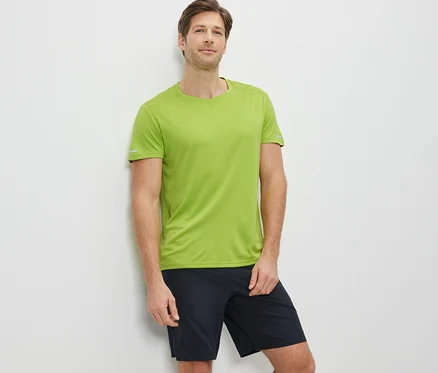 Mann lehnt an der Wand und trägt ein limefarbenes Funktionsshirt und schwarze Shorts.