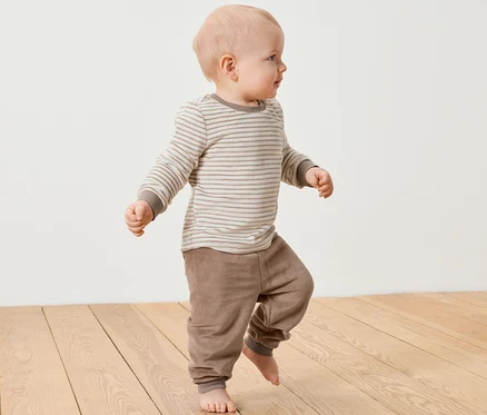 Ein Baby geht auf einem Holzboden und trägt ein Baby-Nicki-Set.