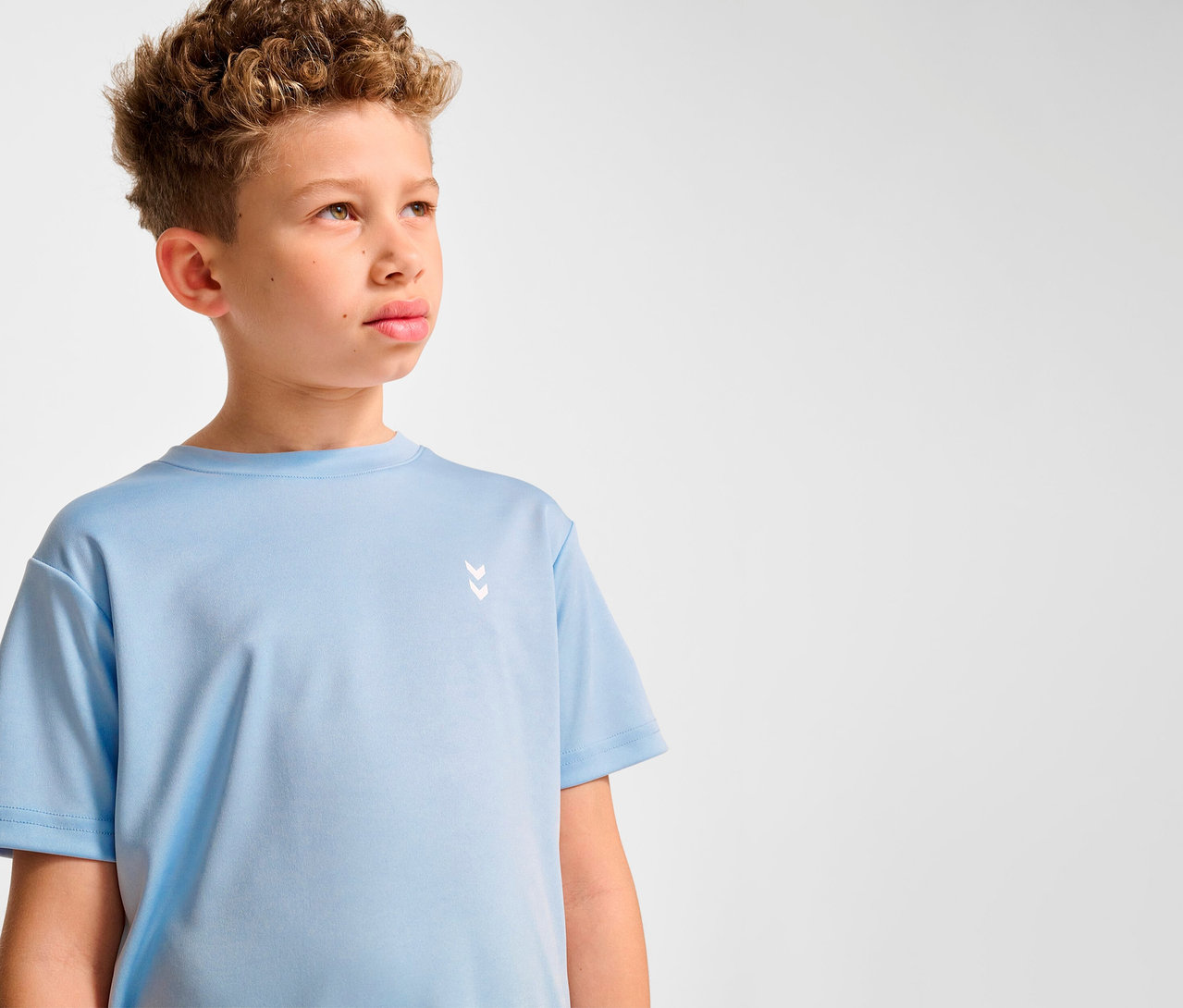 Junge mit lockigem Haar trägt ein hellblaues HUMMEL HMLJR pulse Training-T-Shirt.