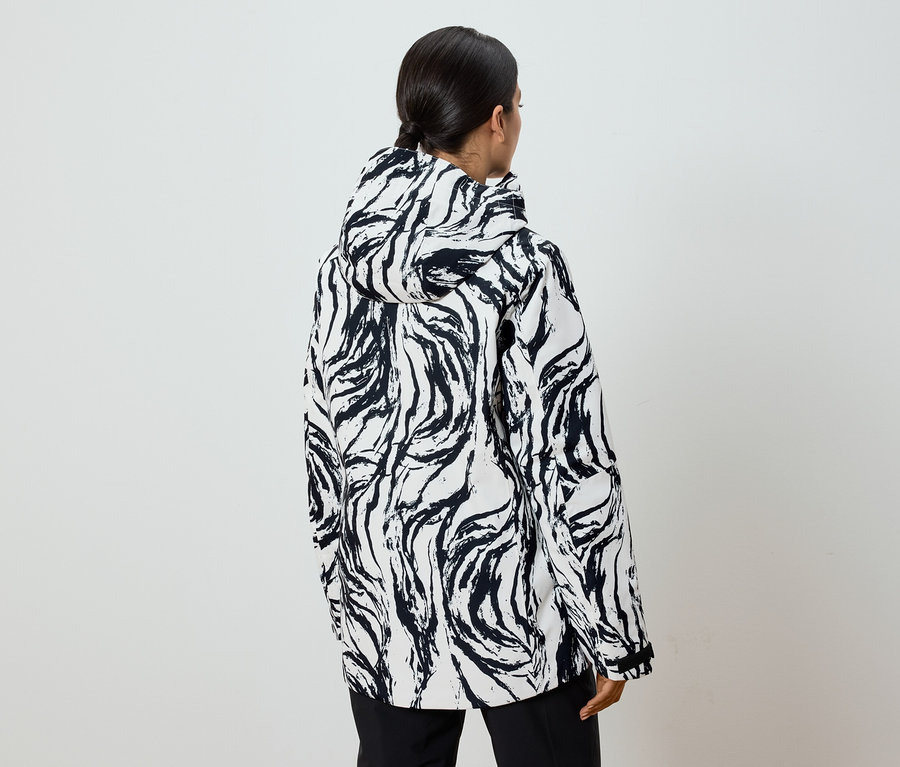 Rückansicht einer Frau mit Pferdeschwanz, die eine schwarz-weiß gemusterte Jacke mit Kapuze trägt.