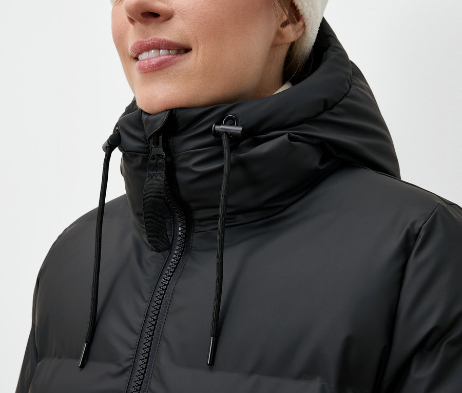 Frau trägt eine schwarze Daunenjacke und eine weiße Mütze.