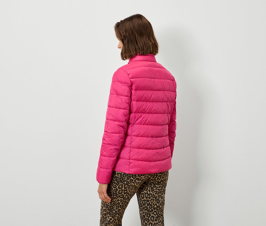 Frau mit dem Rücken zur Kamera trägt eine pinke Steppjacke und eine Hose mit Leopardenmuster.