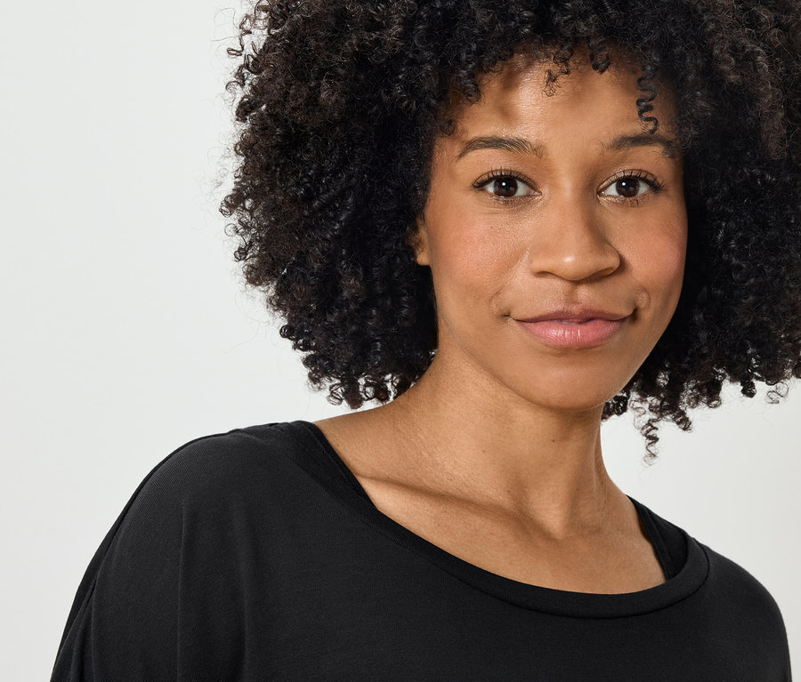 Porträt einer lächelnden Frau mit lockigem Haar in einem schwarzen T-Shirt.