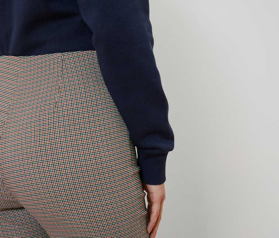 Von hinten trägt eine Frau einen blauen Pullover und eine karierte Hose.