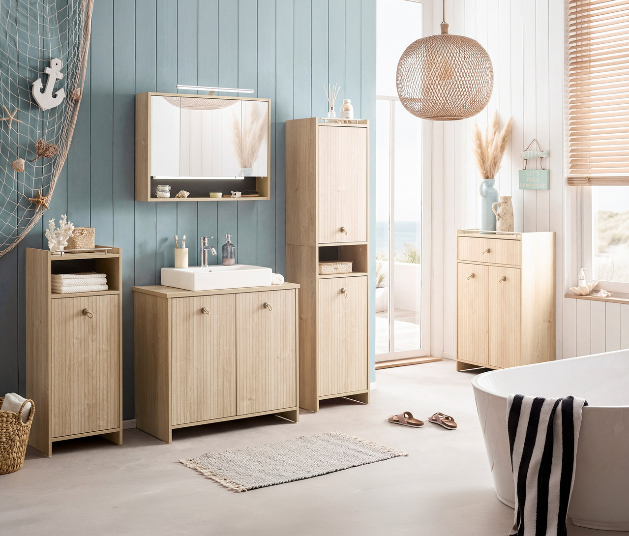 Badezimmer mit Waschtisch, Spiegelschrank, Hochschrank und Badewanne. Dekoriert mit maritimen Elementen wie Anker und Muscheln.