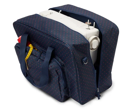 Eine weiße Nähmaschine in einer offenen marineblauen Tasche mit roten Herzen. Ein gelbes Maßband ist an der Außentasche befestigt.