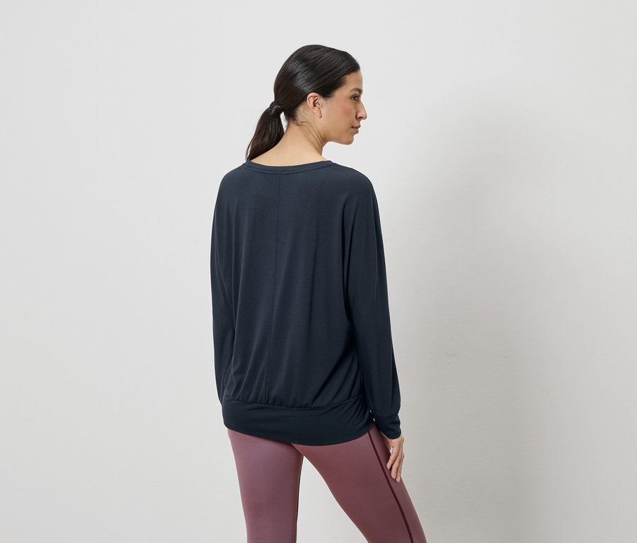 Frau von hinten in einem dunkelblauen Langarmshirt und violetten Leggings.