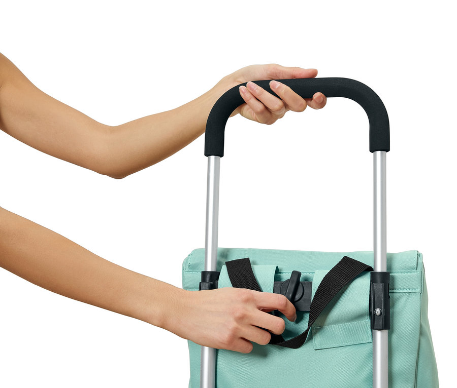 Eine Person befestigt eine hellblaue Tasche mit schwarzen Gurten an einem Trolley mit silbernen Stangen und einem schwarzen Griff.