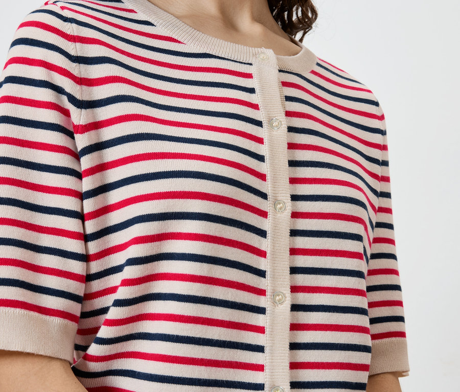 Nahaufnahme einer Frau, die eine gestreifte, kurzärmlige Strickjacke mit Knöpfen in Rot, Marineblau und Beige trägt.