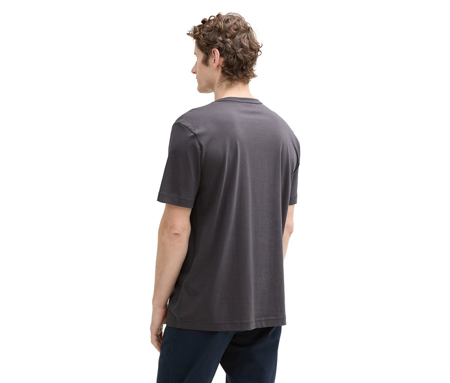 Mann mit lockigem Haar von hinten, trägt ein graues T-Shirt und eine dunkle Hose.