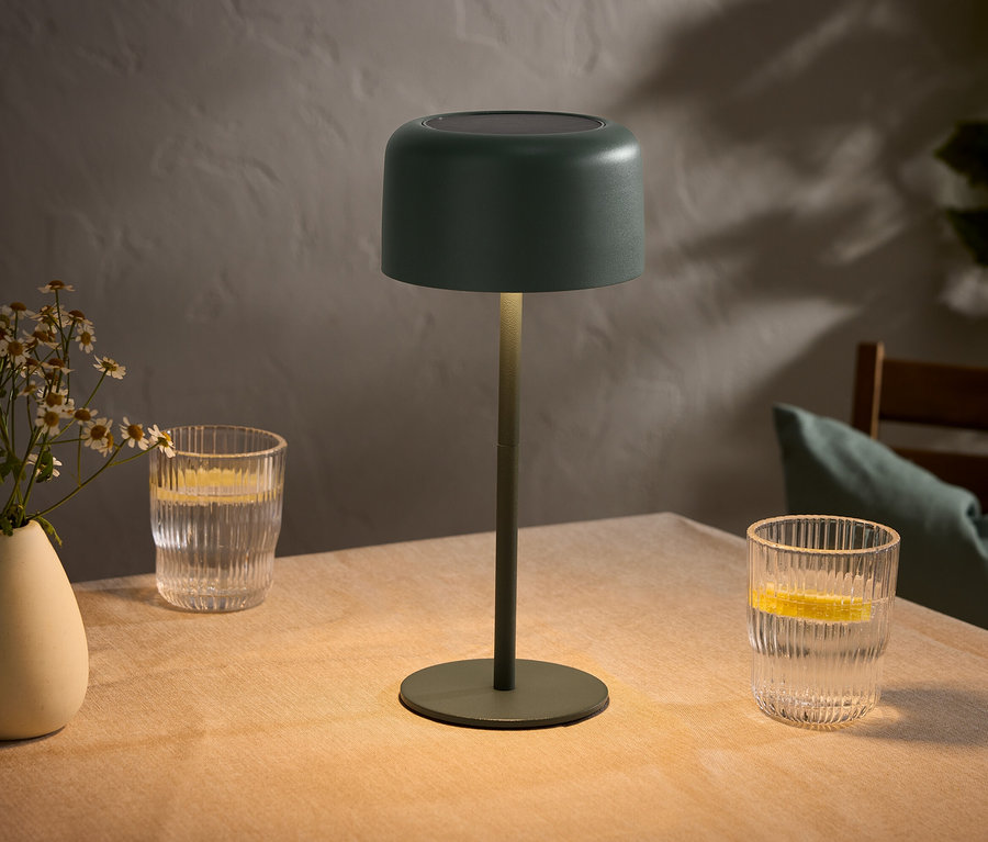 Tisch mit Blumenvase, zwei Gläsern mit Zitronen und einer grünen Lampe.