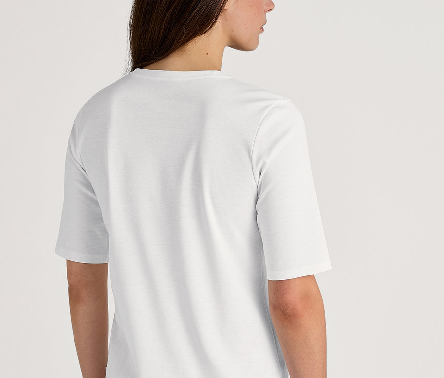 Rückansicht einer Frau mit langen, dunklen Haaren, die ein weißes T-Shirt und eine rosa-schwarz gestreifte Pyjamahose trägt.