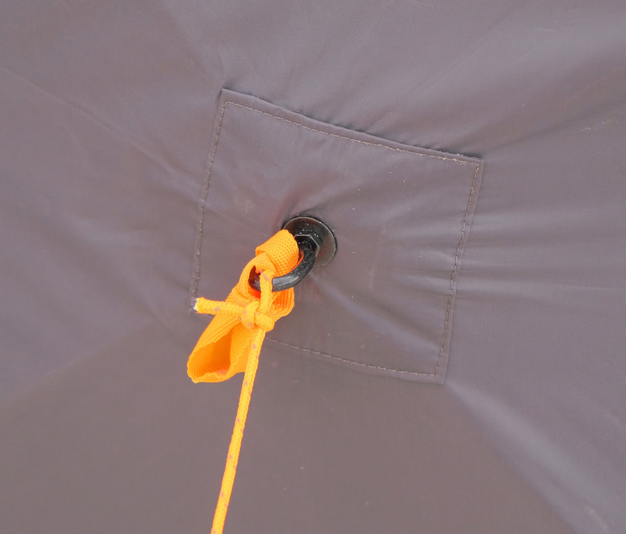Nahaufnahme eines Zeltes mit einer orangefarbenen Abspannleine, die an einer schwarzen Öse befestigt ist.
