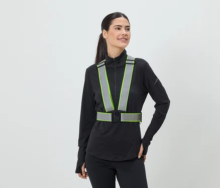 Frau mit Pferdeschwanz trägt eine reflektierende Sicherheitsweste mit neongrünen Akzenten über einem schwarzen Sportoberteil.