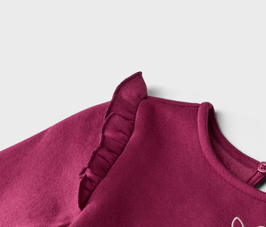 Nahaufnahme eines burgunderroten Sweatshirts mit Rüschen an der Schulter und Knopf am Nacken.