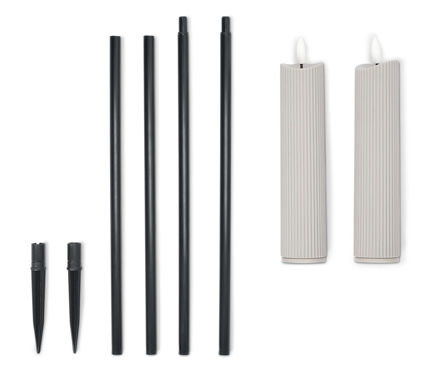 Zwei cremefarbene Kerzen mit vier schwarzen Stäben und zwei Erdspießen liegen aufgereiht auf einem weißen Hintergrund.
