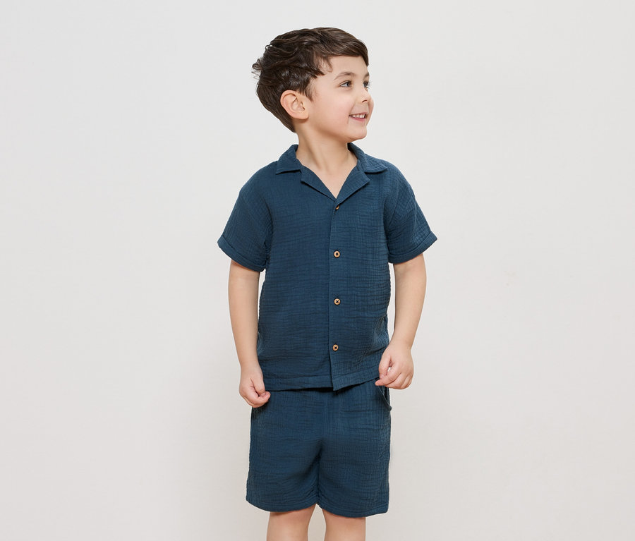 Ein Junge trägt ein marineblaues Hemd mit Knöpfen und dazu passende Shorts.